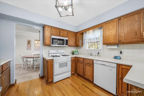 a kitchen with stainless steel appliances granite countertop a stove top oven a sink dishwasher a dining table and chairs with wooden floor