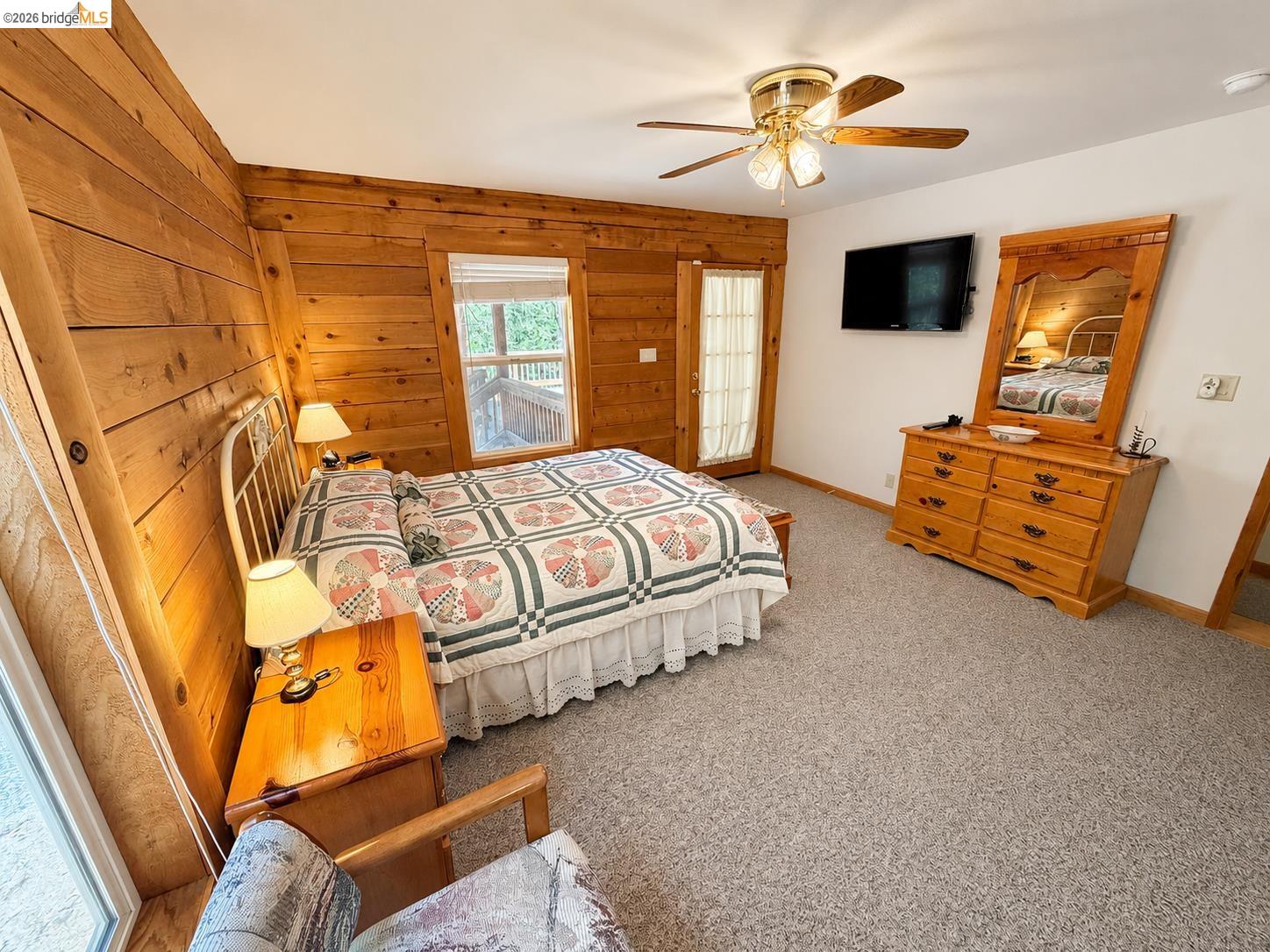 21181 Phoenix Lake Road Sonora, CA 95370 - Photo 24 of 34 Wood-paneled room featuring light-colored carpeting, a ceiling fan with light fixture, a window with blinds, a glass-paned door, and a wall-mounted flat-screen television