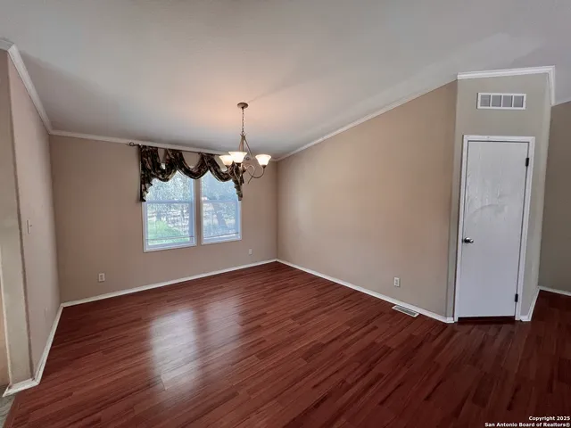 an empty room with wooden floor chandelier and windows