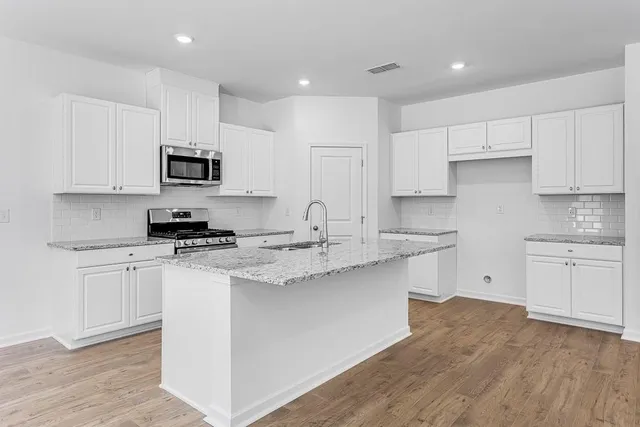 a kitchen with stainless steel appliances granite countertop a sink a stove a refrigerator and white cabinets