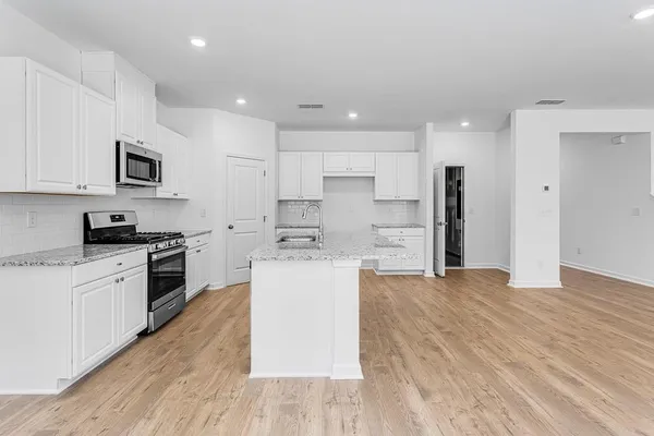 a kitchen with stainless steel appliances kitchen island granite countertop a stove a sink and white cabinets