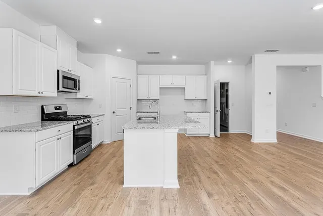 a kitchen with stainless steel appliances kitchen island granite countertop a stove a sink and white cabinets