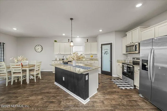 a kitchen with stainless steel appliances kitchen island granite countertop a table chairs and a refrigerator