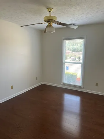 an empty room with wooden floor chandelier fan and windows