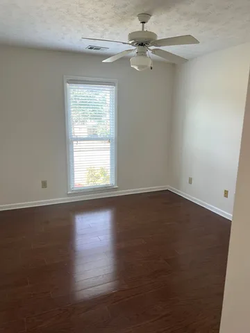 an empty room with wooden floor fan and windows