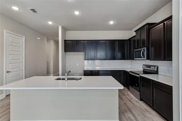 a kitchen with stainless steel appliances a sink dishwasher a refrigerator and a stove with wooden floor