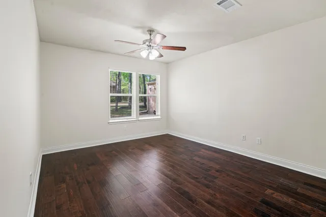 an empty room with wooden floor chandelier fan and windows