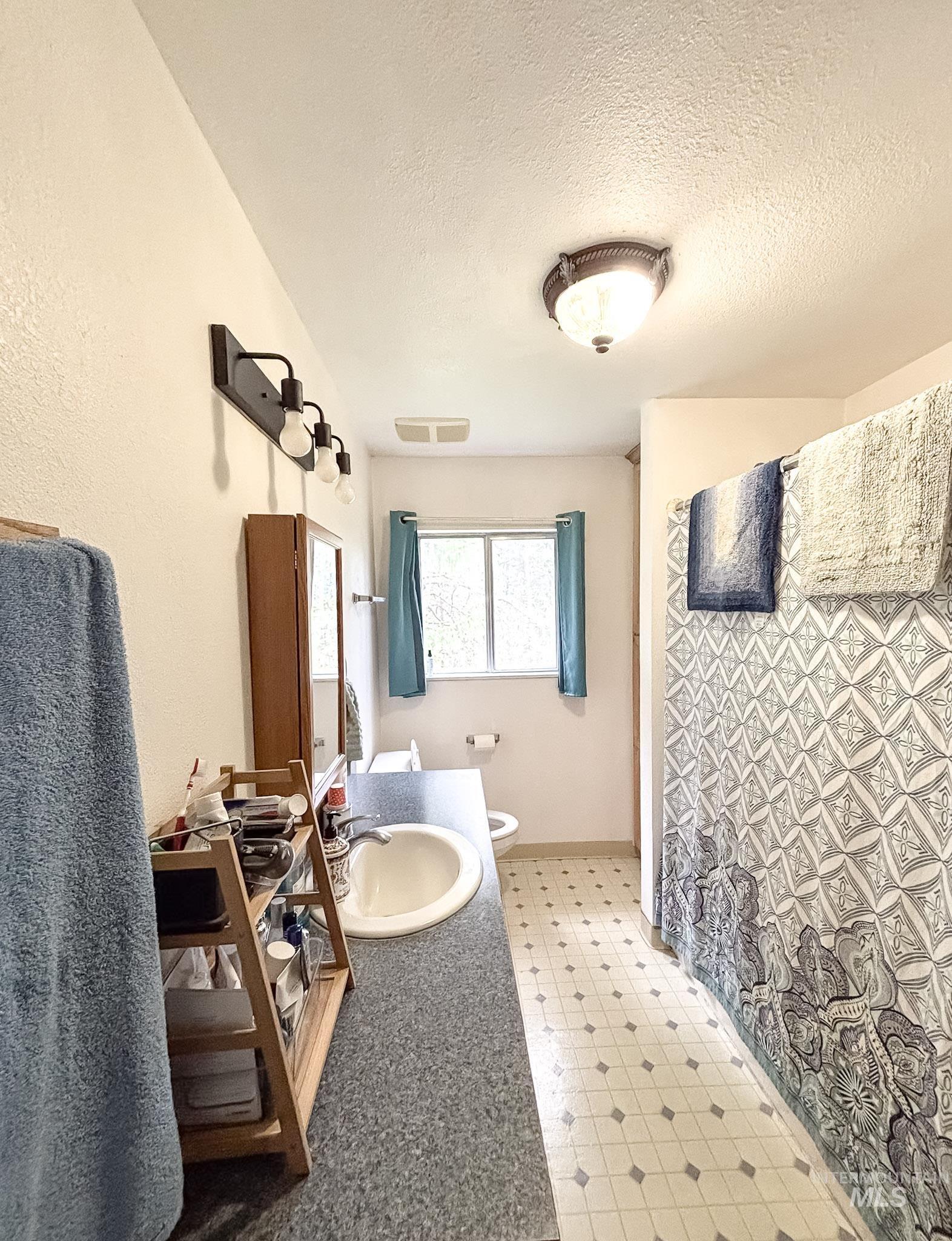 1650 Wells Bench Road Orofino, ID 83544 - Photo 18 of 44 Bathroom featuring a single basin vanity with a speckled countertop, a three-light fixture, a built-in medicine cabinet, and a window with teal curtains