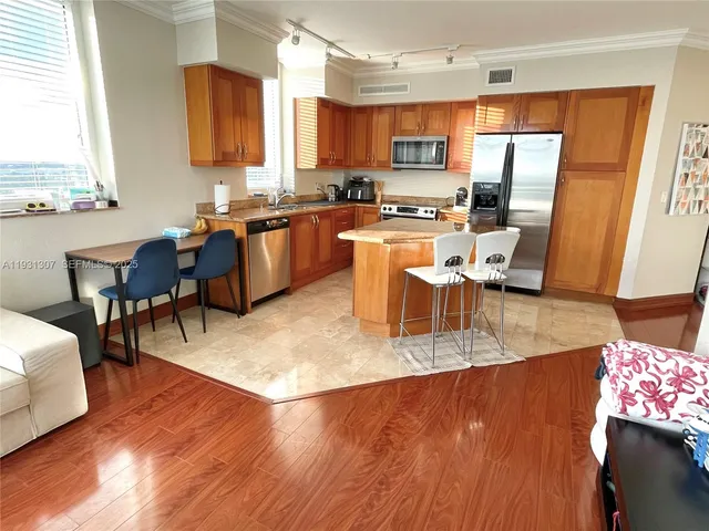 a kitchen with stainless steel appliances granite countertop a stove top oven a sink a dining table and chairs with wooden floor