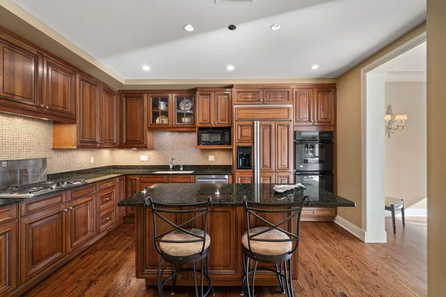 a kitchen with stainless steel appliances granite countertop wooden cabinets a refrigerator a stove a sink and dishwasher with wooden floor