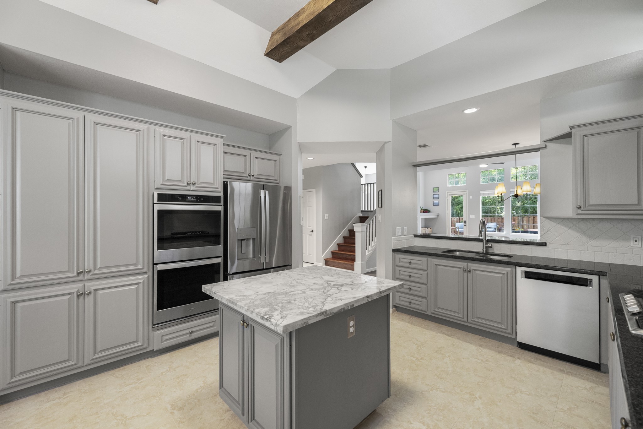 102 Treescape Circle Spring, TX 77381 - Photo 2 of 40 This spacious kitchen features modern gray cabinetry, stainless steel built-in appliances, and an island. It opens to a bright, inviting living area with large windows and a view of the backyard.