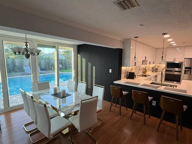 a kitchen with stainless steel appliances granite countertop a refrigerator a stove a sink and a dining table with wooden floor