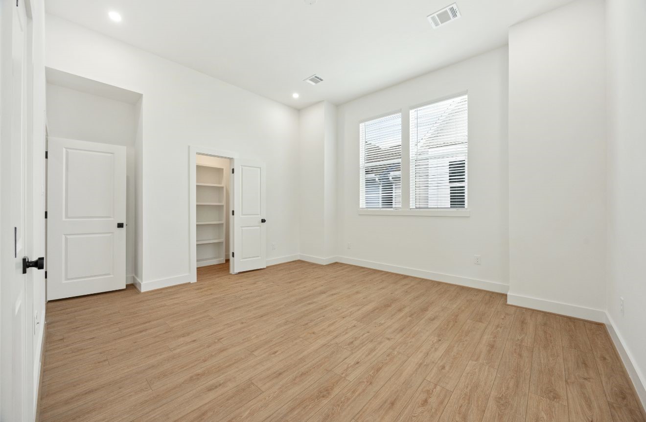2121 Hoskins Drive, Unit C Houston, TX 77080 - Photo 23 of 34 Spacious upper-level bedroom with high ceilings, recessed lighting, warm wood-look flooring, large windows, and a walk-in closet with built-in shelving. The neutral palette and generous proportions create a calm, comfortable retreat ready for a variety of furniture layouts and personal styling.