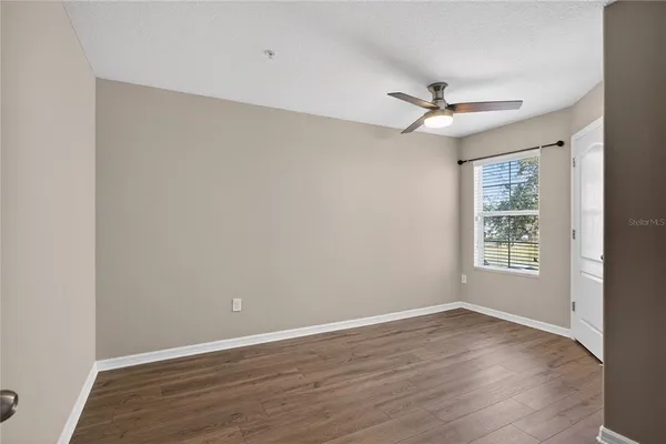 an empty room with wooden floor ceiling fan and windows