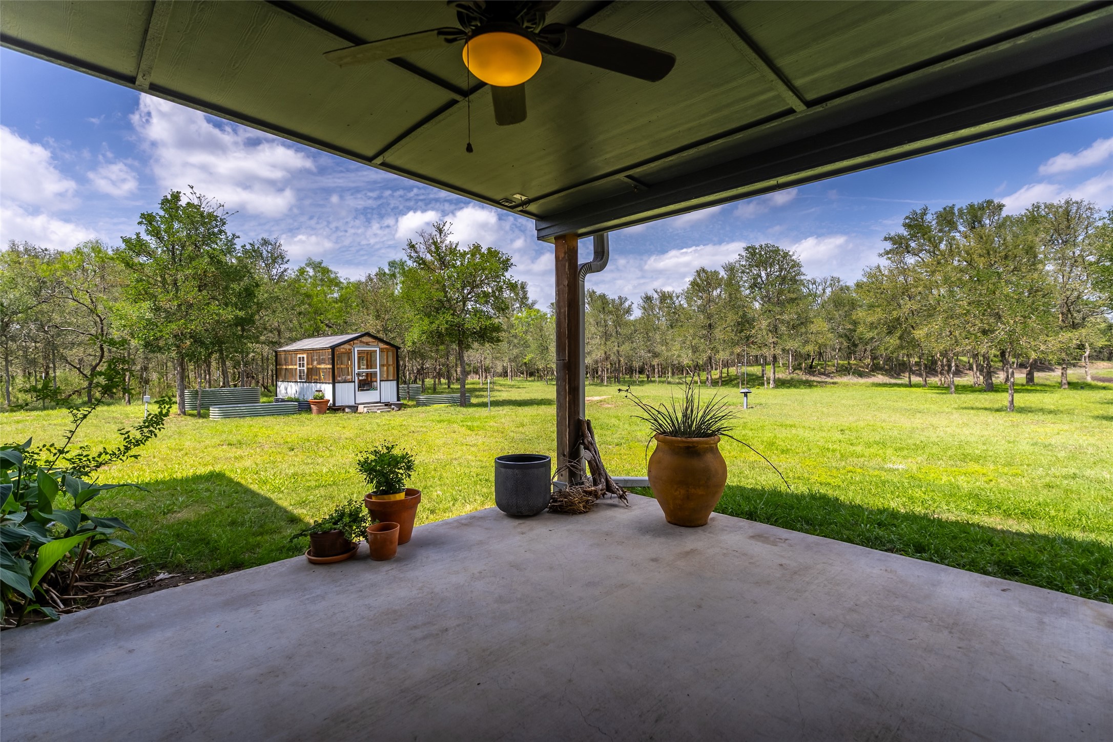 4082 Old Colony Line Road Lockhart, TX 78644 - Photo 14 of 40 An inviting covered patio overlooks a vast, verdant yard with a charming greenhouse and mature trees.