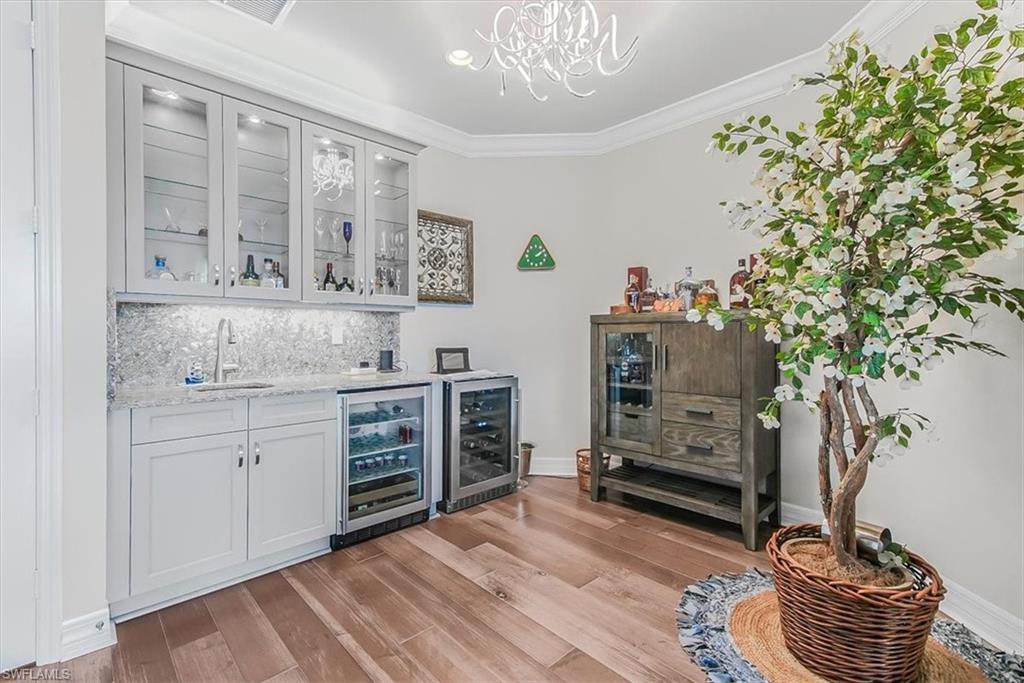 4616 Azalea Drive Naples, FL 34119 - Photo 22 of 44 Indoor wet bar featuring ornamental molding, backsplash, wine cooler, glass insert cabinets, and light wood-style floors