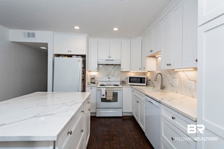 Kitchen featuring white appliances, white cabinets, tasteful backsplash, dark wood-style floors, and recessed lighting