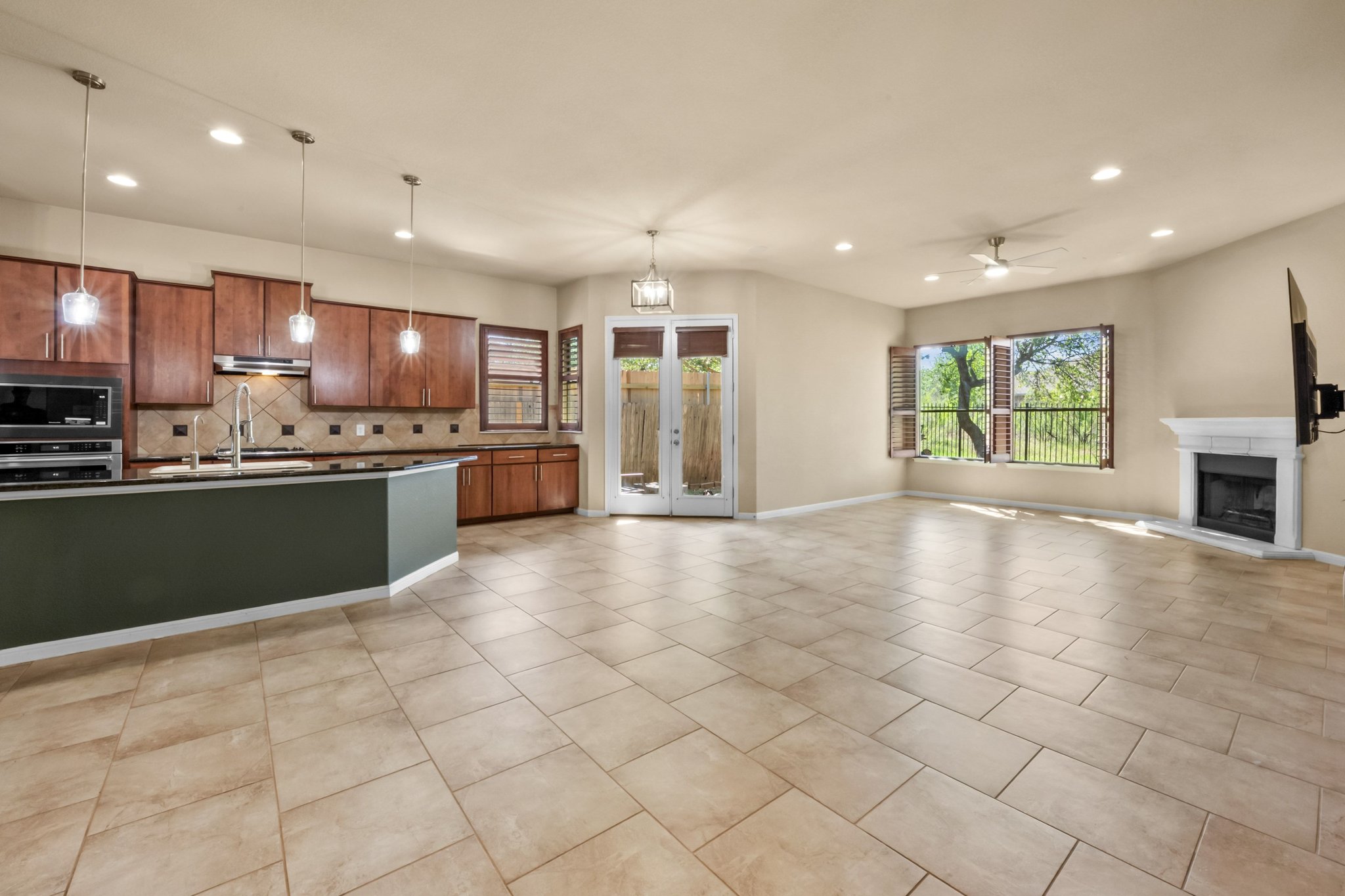 22204 Red Yucca Road Spicewood, TX 78669 - Photo 34 of 34 Kitchen with wood finish cabinetry, open floor plan, ceiling fan, a fireplace with raised hearth, and pendant lighting