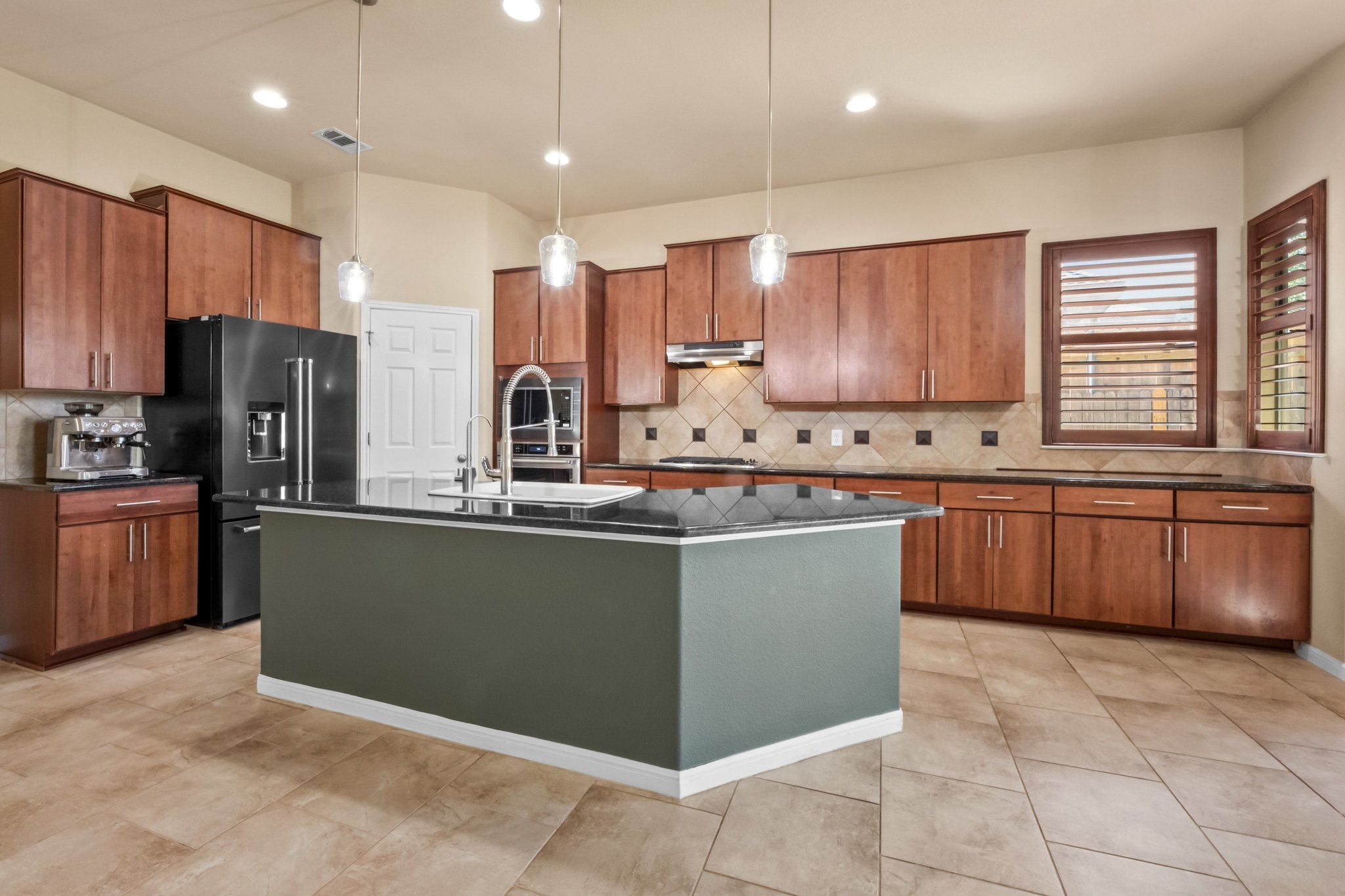 22204 Red Yucca Road Spicewood, TX 78669 - Photo 8 of 34 Kitchen featuring pendant lighting, wood finish cabinets, high end black fridge, and a center island with sink
