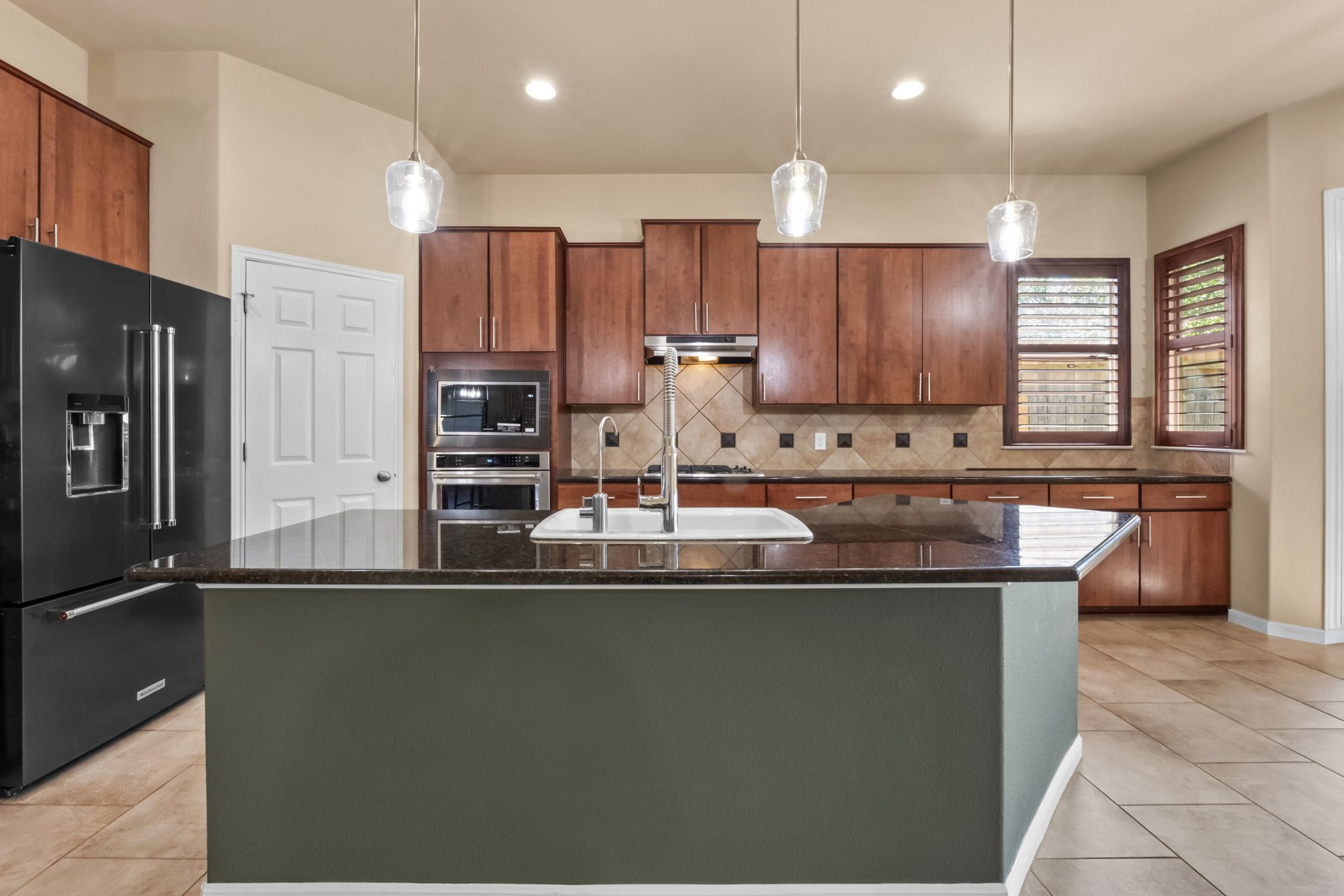 22204 Red Yucca Road Spicewood, TX 78669 - Photo 9 of 34 Kitchen with stainless steel appliances, dark stone counters, a kitchen island with sink, light tile patterned flooring, and wood finish cabinetry