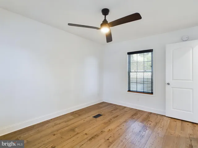 an empty room with wooden floor chandelier fan and windows