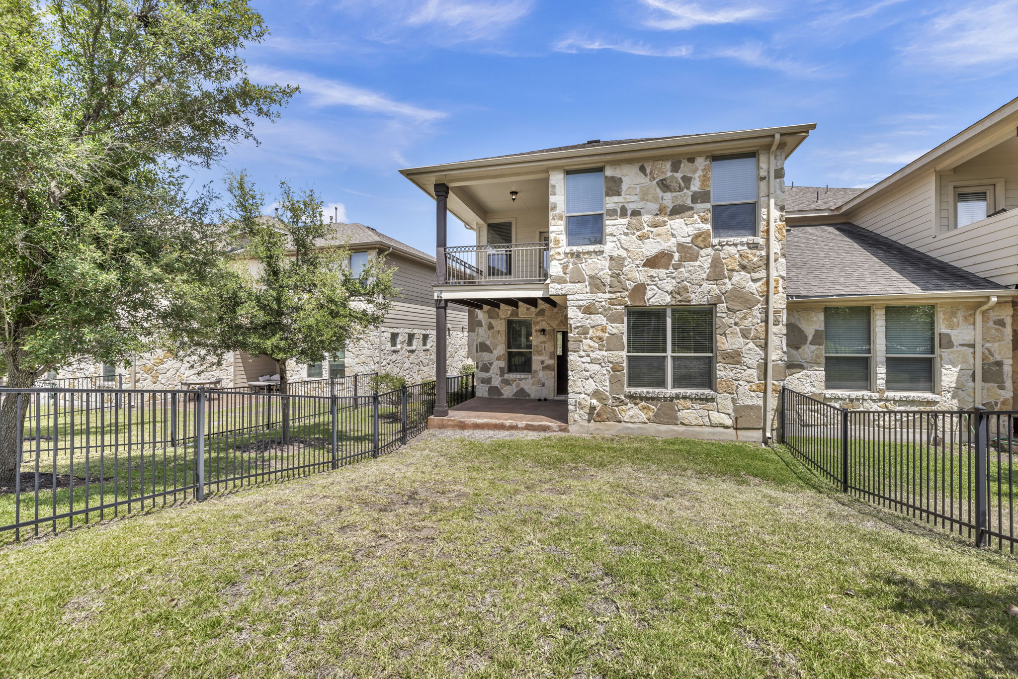 7320 Bandera Ranch Trail, Unit B Austin, TX 78750 - Photo 26 of 27 Rear view of house with stone siding, a balcony, and a fenced backyard
