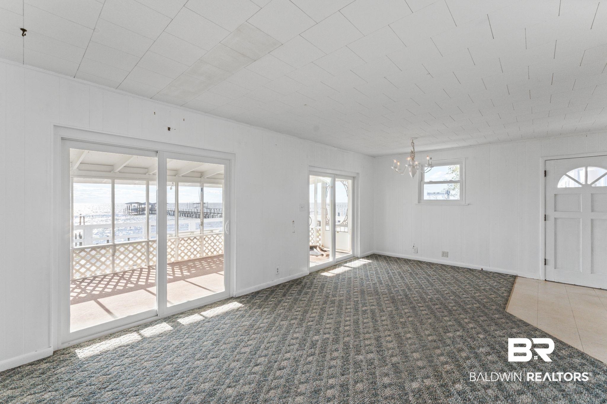 8959 Shore Drive Foley, AL 36535 - Photo 19 of 53 Unfurnished living room with carpet floors, a chandelier, wooden walls, and tile patterned flooring