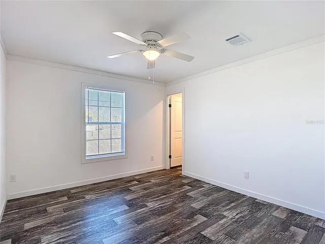 an empty room with wooden floor fan and windows