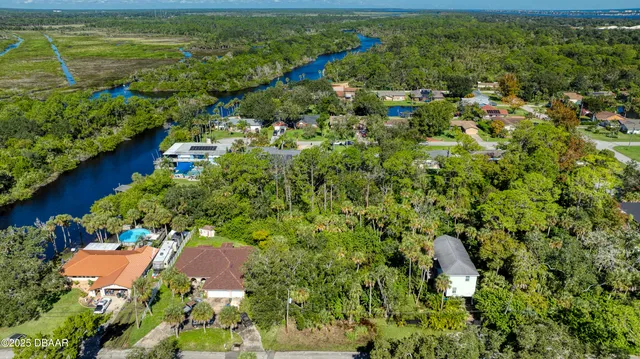 an aerial view of a residential houses with outdoor space and trees all around