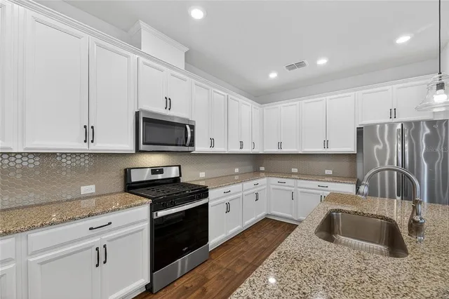 a kitchen with granite countertop a sink stainless steel appliances and white cabinets