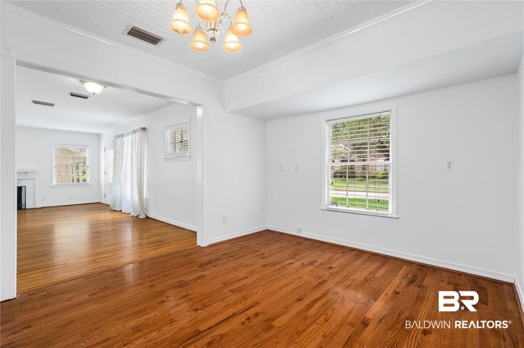 218 Grand Boulevard Mobile, AL 36607 - Photo 19 of 22 Empty room with wood-type flooring, a brick fireplace, an inviting chandelier, and crown molding