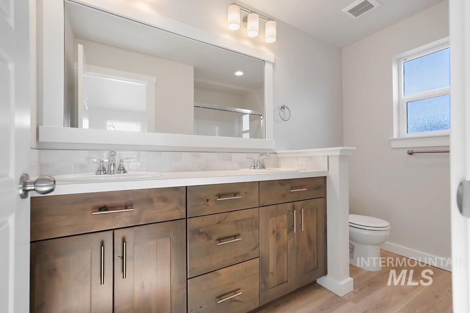 985 Twilight Street Weiser, ID 83672 - Photo 15 of 32 Bathroom with double vanity, light wood-style floors, decorative backsplash, and a stall shower