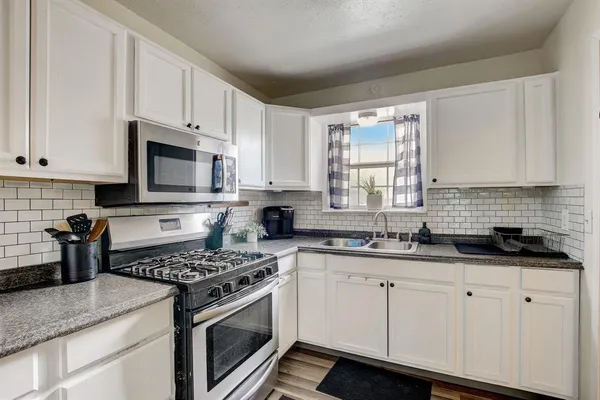 a kitchen with granite countertop white cabinets sink and stainless steel appliances