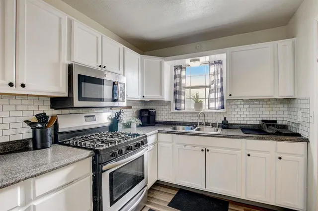 a kitchen with granite countertop white cabinets sink and stainless steel appliances