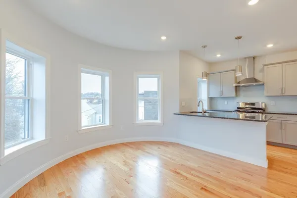 a open kitchen with granite countertop a stove top oven a sink and white cabinets with wooden floor