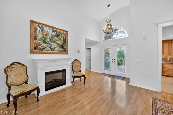 43 Grey Wing Point Naples, FL 34113 - Photo 22 of 50 Foyer entrance with french doors, high vaulted ceiling, a glass covered fireplace, light wood-style floors, and a chandelier