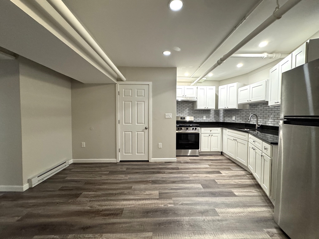 a large kitchen with kitchen island granite countertop a stove top oven a sink and white cabinets