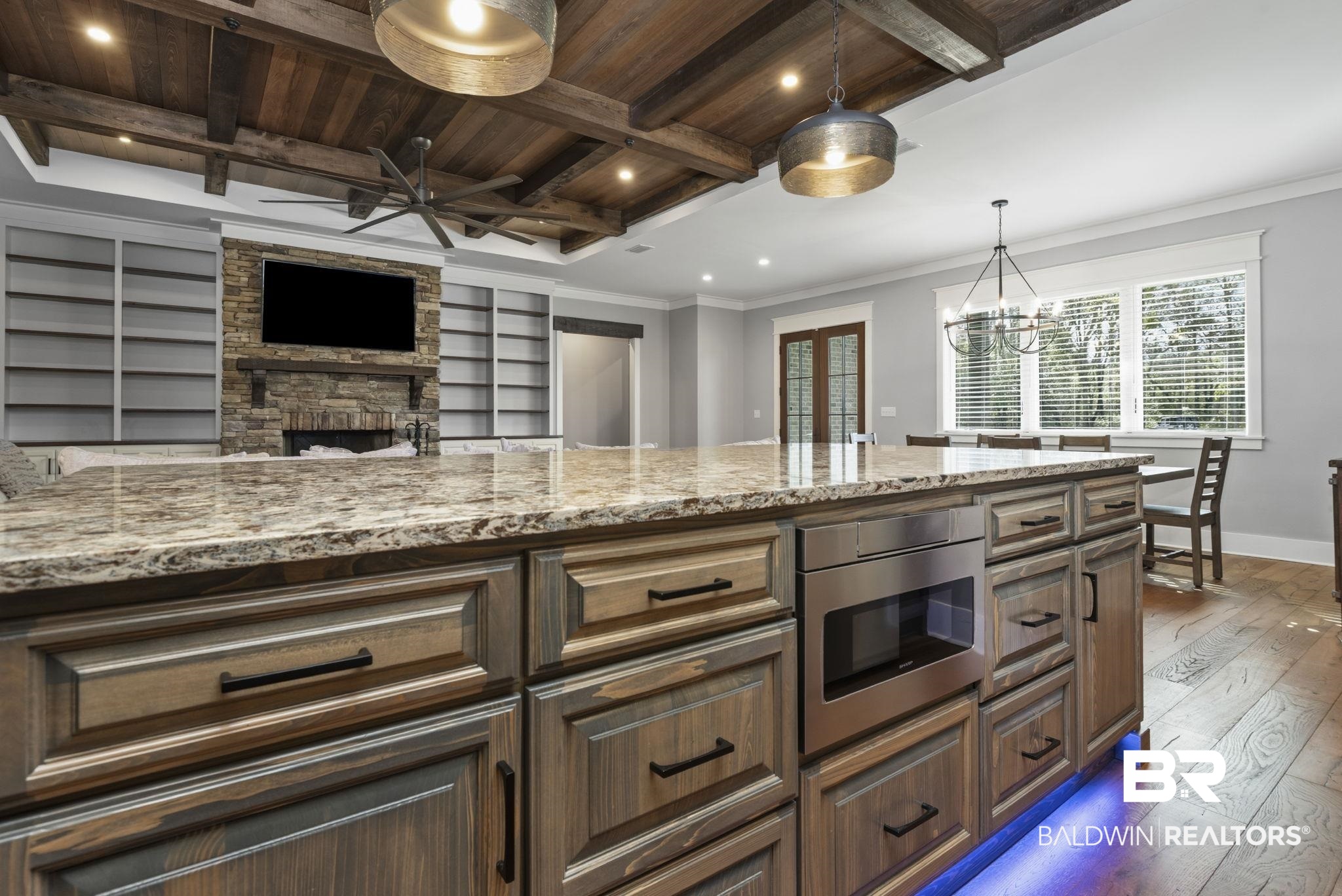 9501 Ben Hamilton Road Theodore, AL 36582 - Photo 16 of 69 Kitchen with dark wood finished floors, a fireplace, light stone countertops, stainless steel microwave, and wooden ceiling