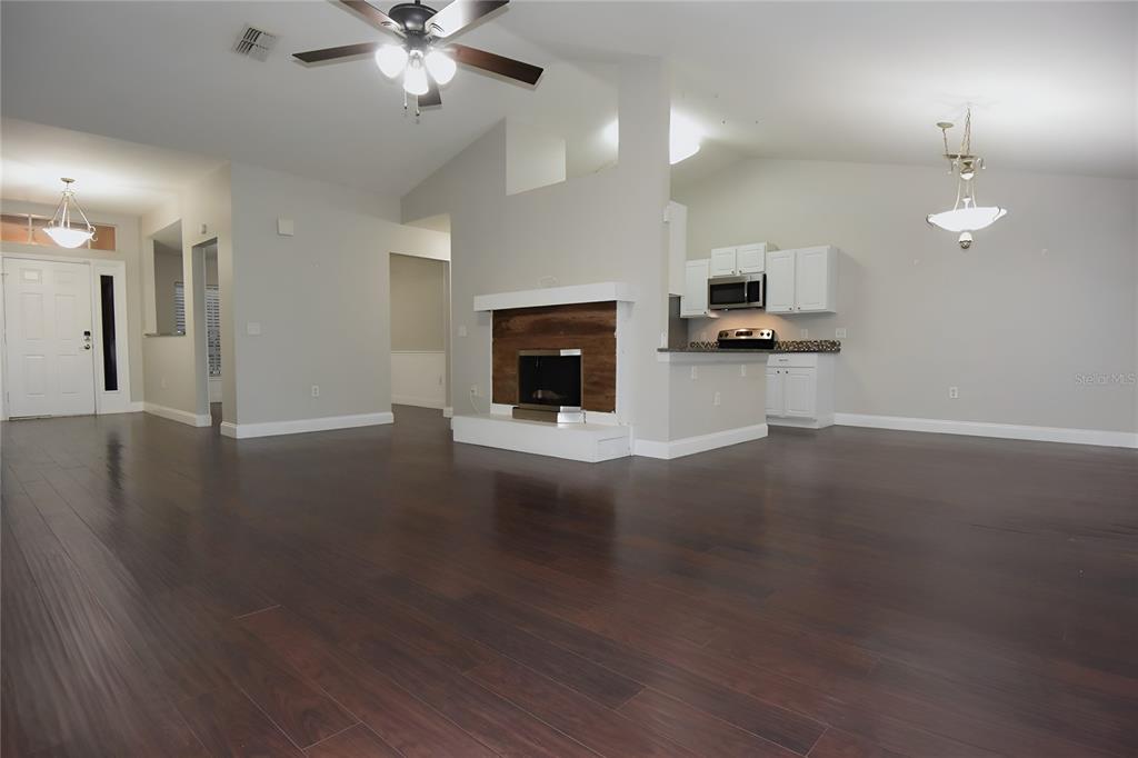 12042 Linden Drive Spring Hill, FL 34608 - Photo 11 of 41 an empty room with wooden floor fireplace and kitchen view