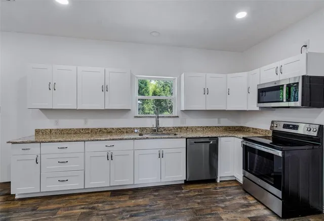 a kitchen with granite countertop white cabinets white stainless steel appliances and a sink