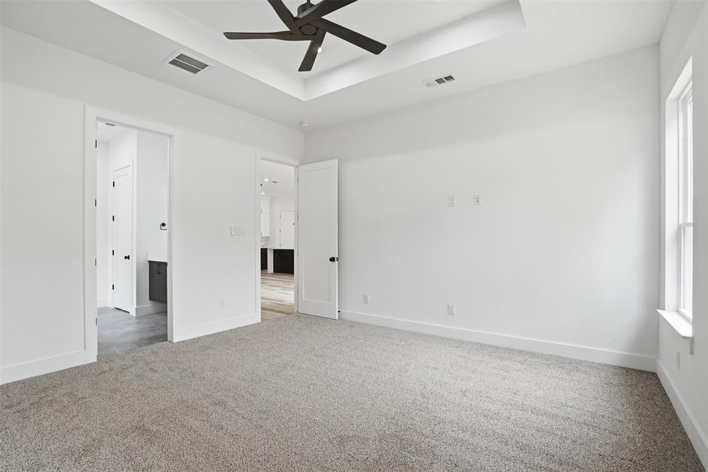 1111 Riverwood Road Dallas, TX 75217 - Photo 21 of 40 Spacious room with gray carpeting, a tray ceiling featuring a dark-toned ceiling fan, and white walls