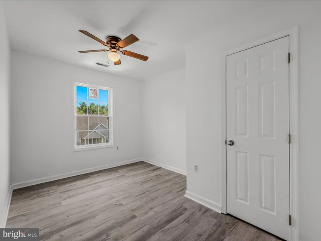 an empty room with wooden floor closet ceiling fan and windows
