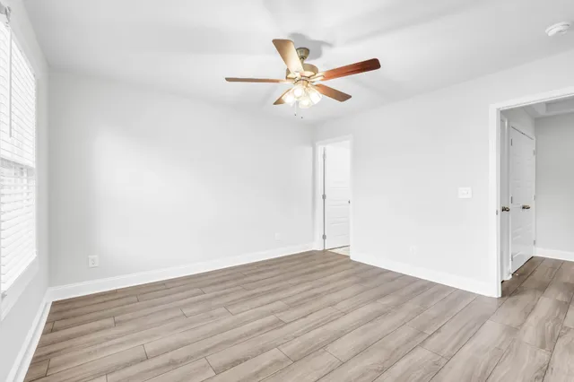 an empty room with wooden floor fan and windows
