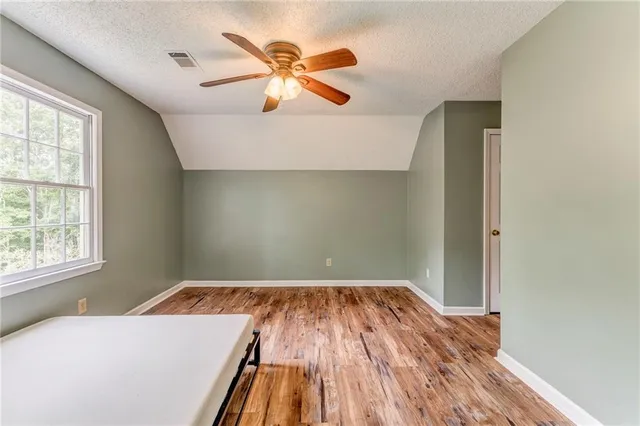 an empty room with wooden floor chandelier fan and windows