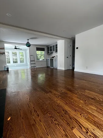 a view of empty room with wooden floor and kitchen view