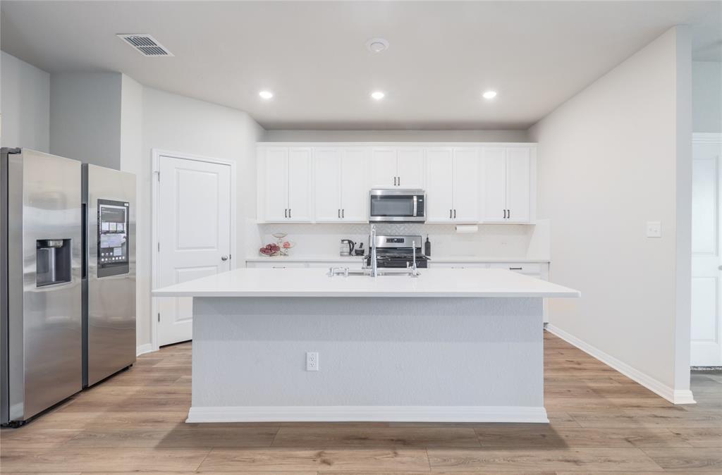 2815 Haystack Lane Round Rock, TX 78665 - Photo 9 of 30 Kitchen featuring appliances with stainless steel finishes, white cabinetry, light wood-type flooring, a center island with sink, and recessed lighting