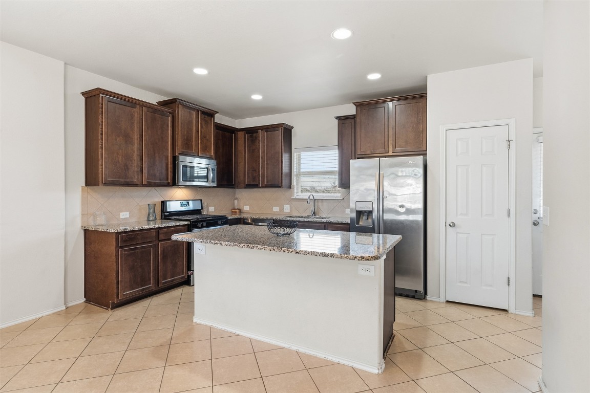 160 Albatross Cove Buda, TX 78610 - Photo 6 of 36 a kitchen with kitchen island granite countertop white cabinets and stainless steel appliances