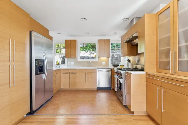 a large kitchen with a refrigerator a sink dishwasher stove and white cabinets with wooden floor