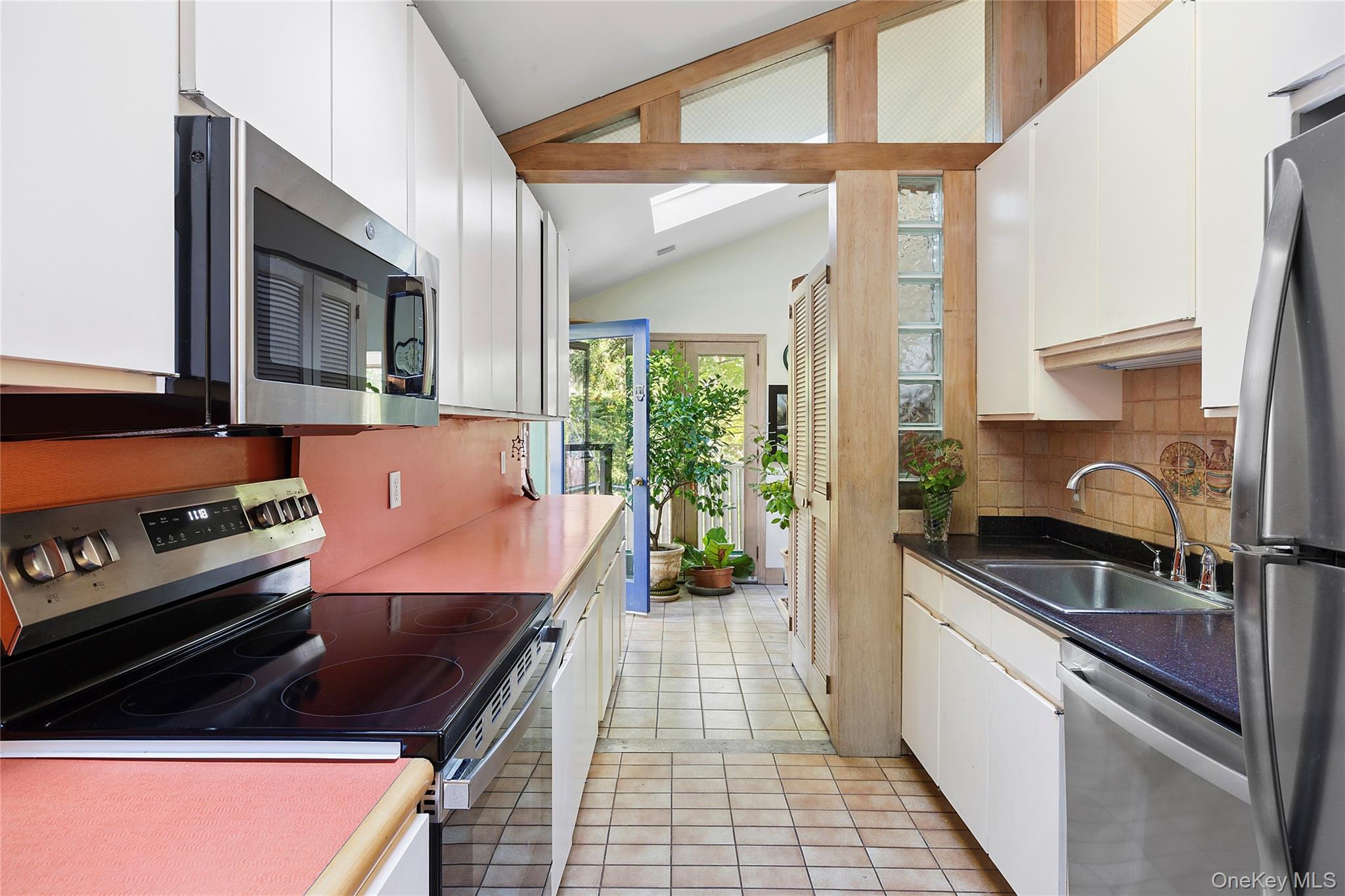 3700 Haywaters Road Cutchogue, NY 11935 - Photo 8 of 22 Kitchen with stainless steel appliances, white cabinetry, vaulted ceiling, light tile patterned flooring, and backsplash