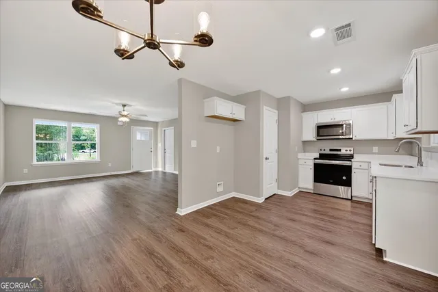 an empty room with wooden floor ceiling fan and kitchen view